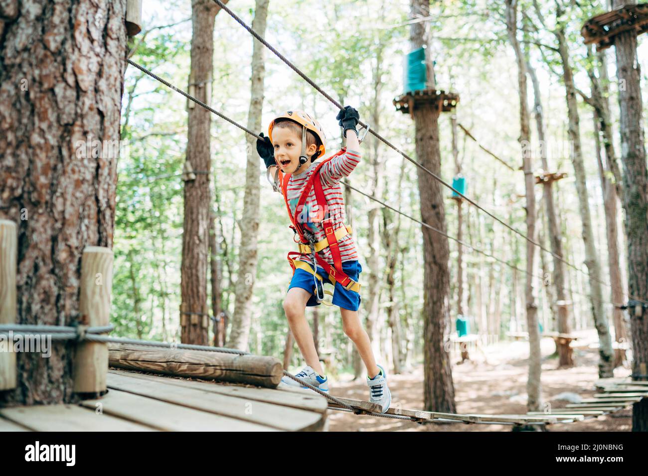 Boy walks across the agility bridge to a platform on a tree Stock Photo