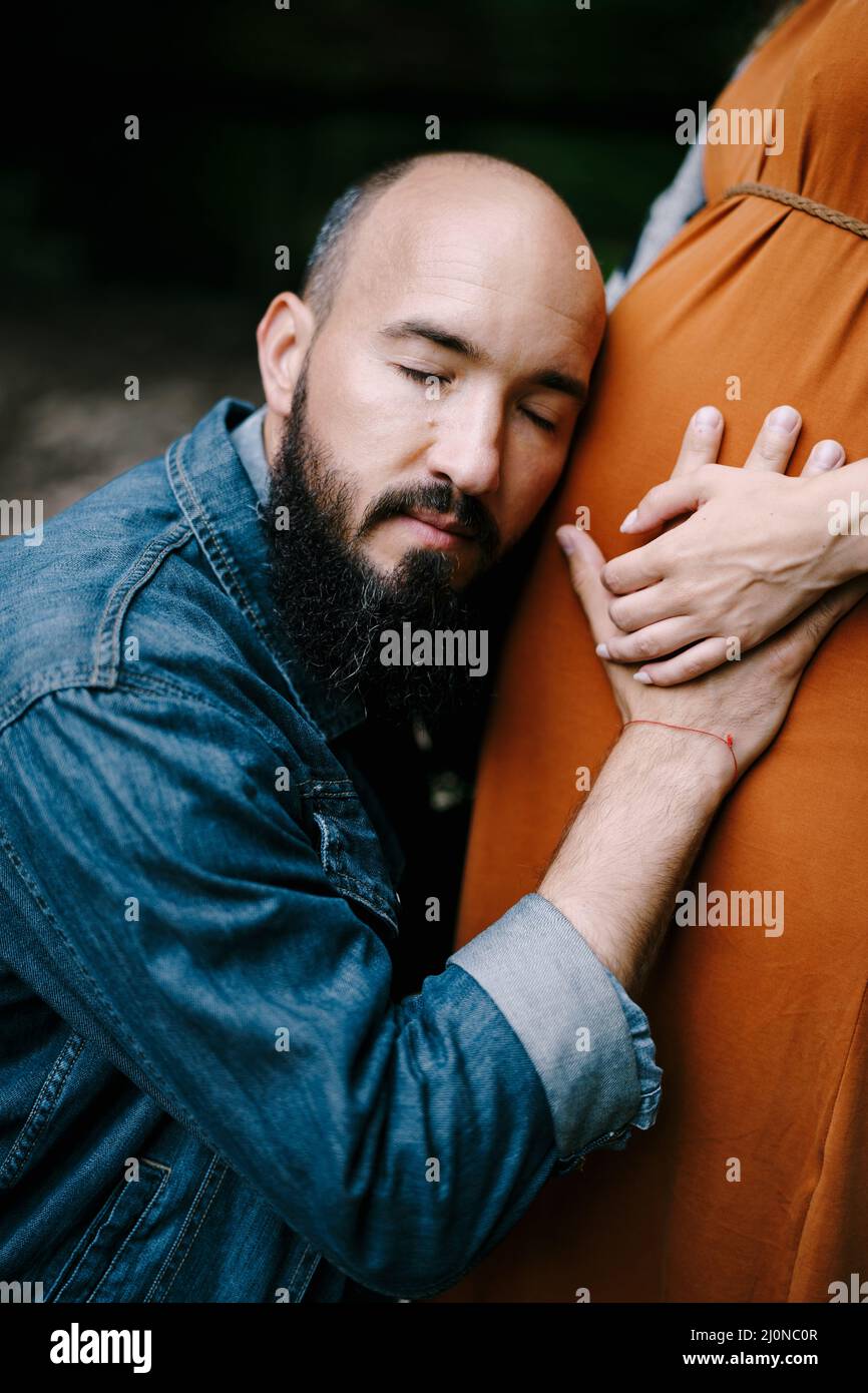 Man hugs woman pregnant belly, leaning his ear against it Stock Photo ...