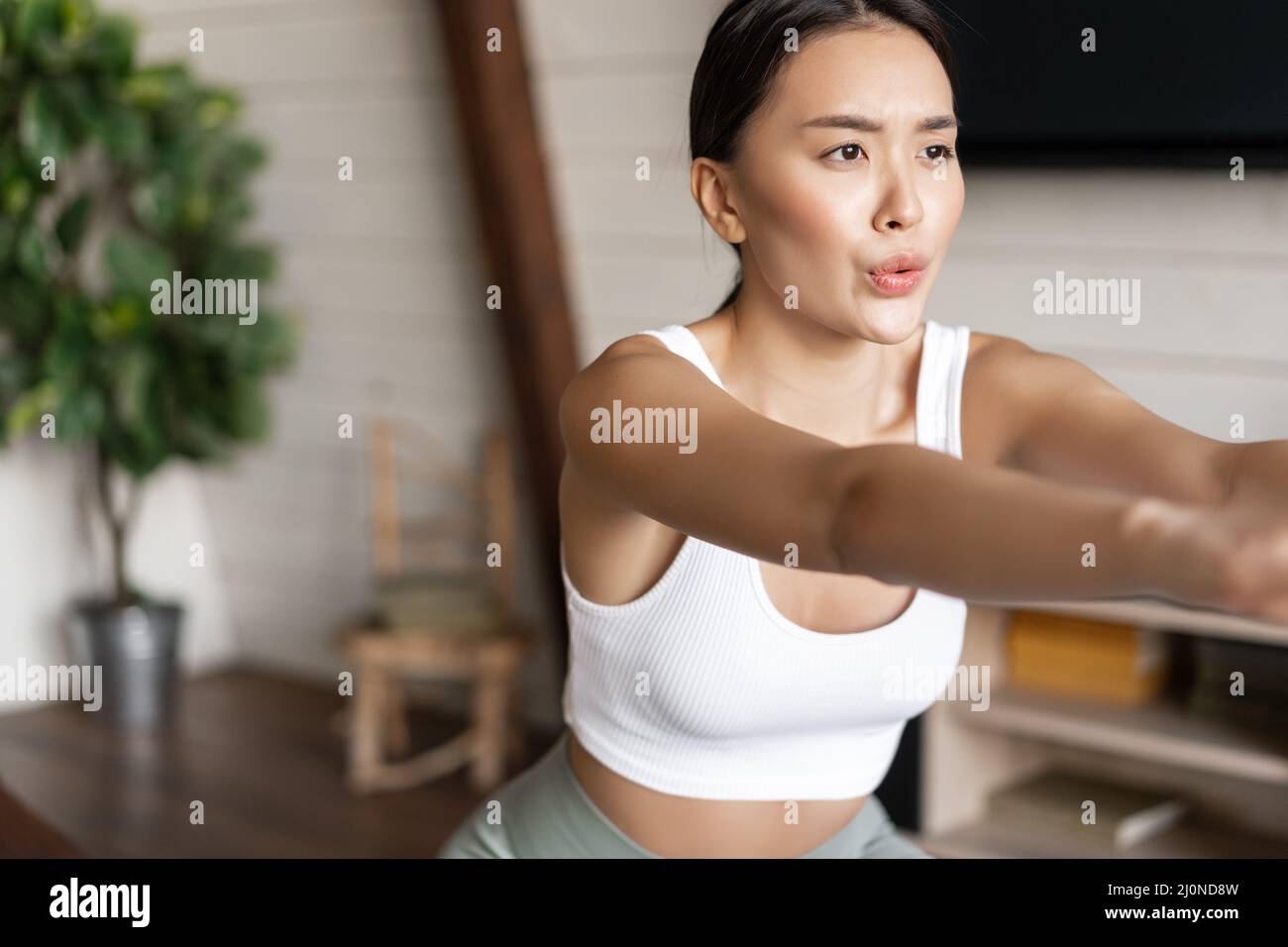 Young asian fitness woman with healthy fit body, doing squats, morning workout, wearing activewear, standing at home in living r Stock Photo