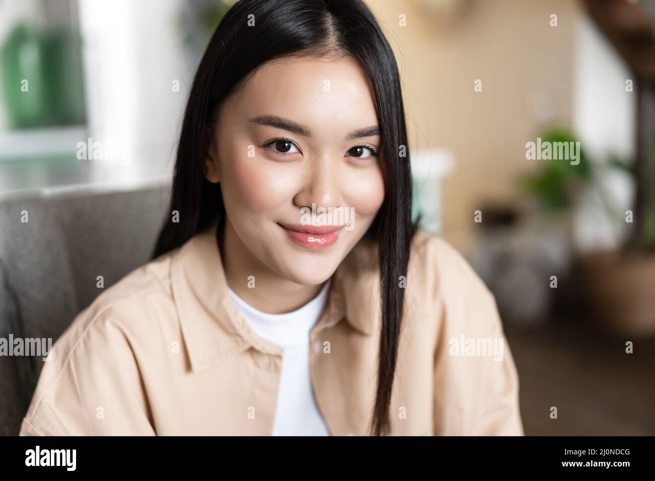 Close up portrait of smiling asian girl looking happy at camera, sitting at home indoors. Face of young woman with joyful emotio Stock Photo