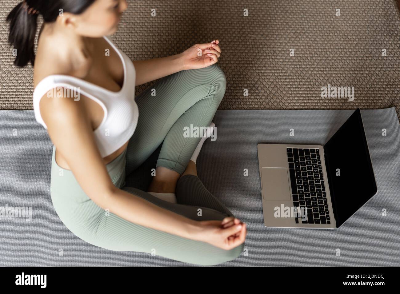 Cropped shot of asian woman meditating in floor mat at home, listening to meditation podcast on laptop, practice yoga online cou Stock Photo