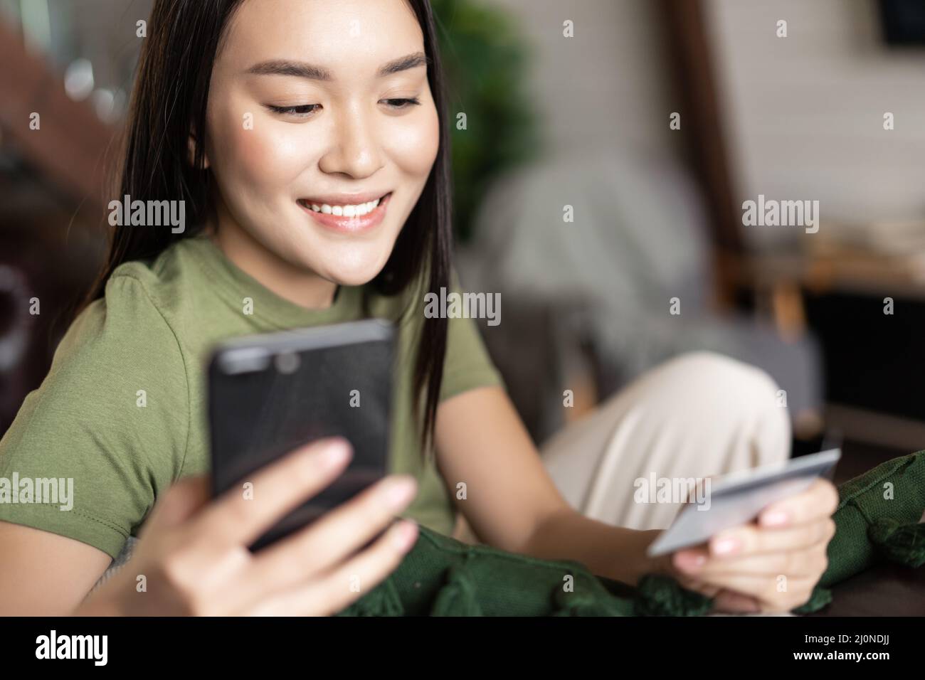 Young asian woman buying from online shop, using mobile phone and credit card, shopping from home Stock Photo