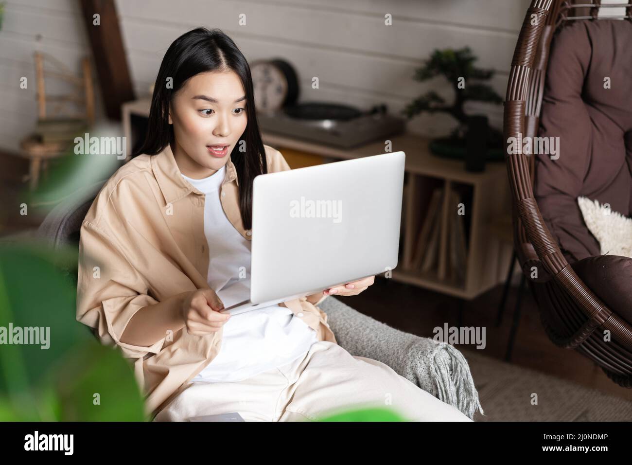 Asian woman looks excited and amazed at laptop screen, winning online, sitting at home Stock Photo
