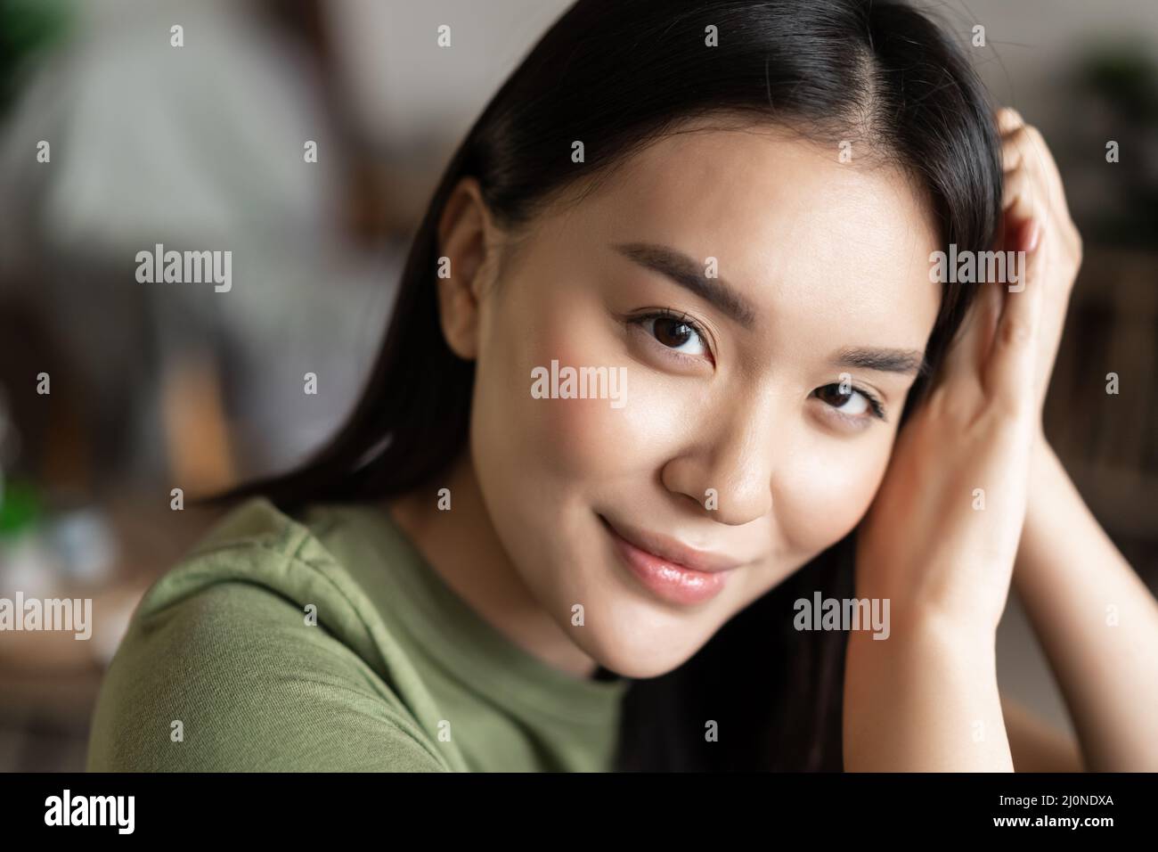 Close up portrait of tender asian girl with glowing natural skin, smiling sensual at camera, sitting at home in cozy clothes Stock Photo