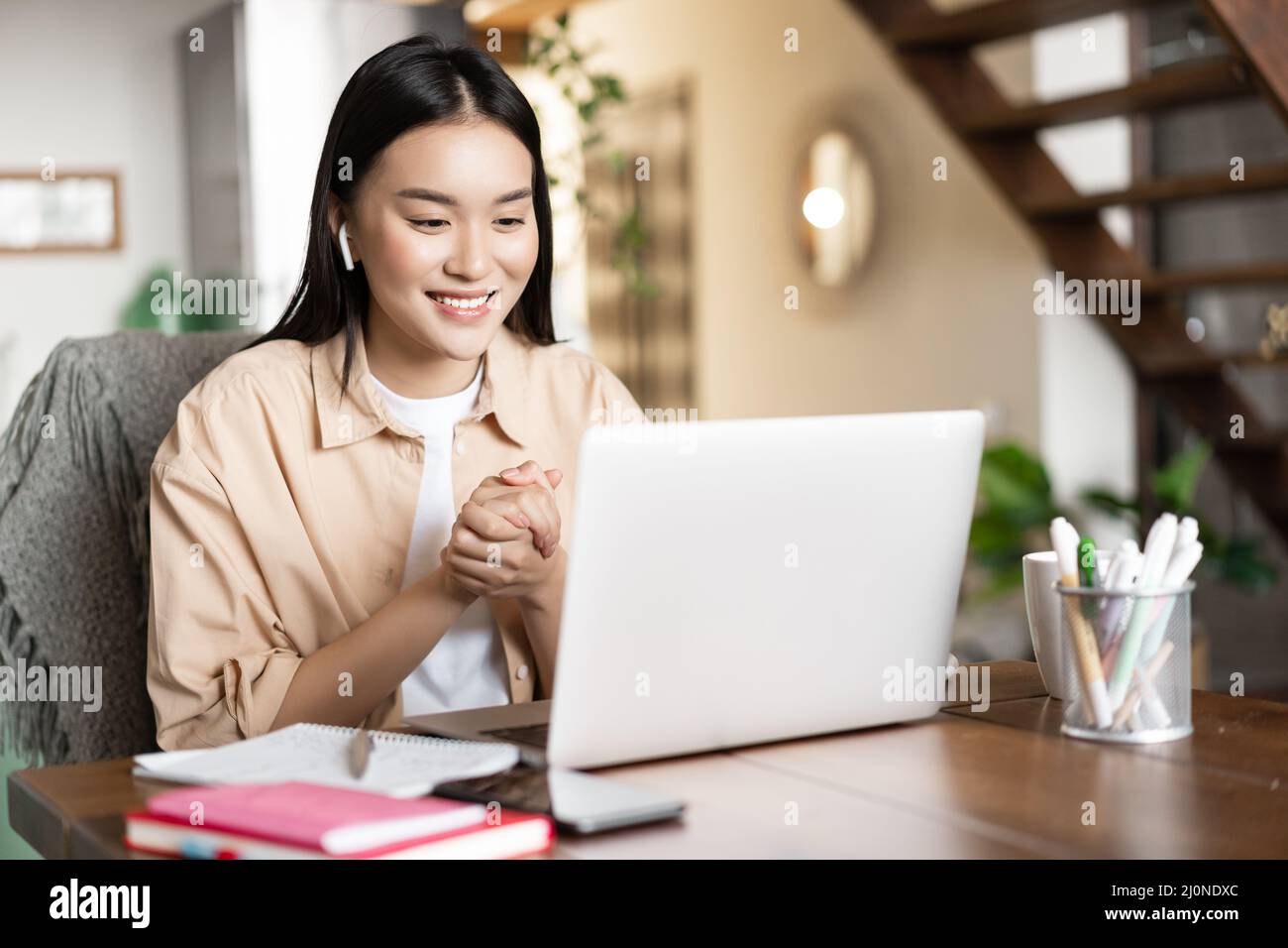 Asian girl studies at home using laptop computer. Young woman attends online classes, webinar or video conference, working on pc Stock Photo