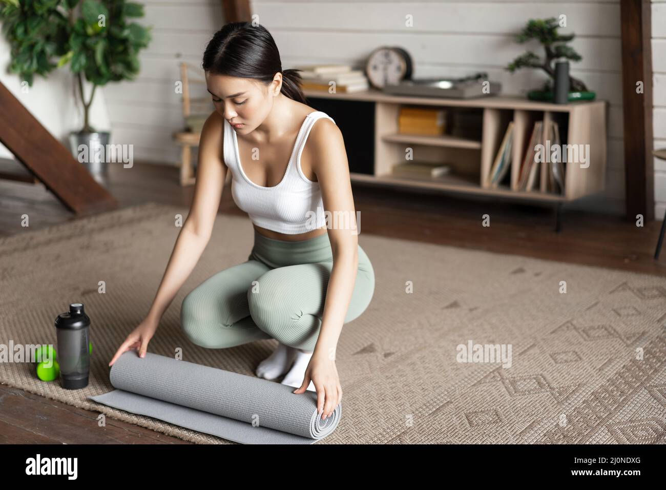 Asian fitness girl finish training,workout at home, rolling floor mat after exercising in living