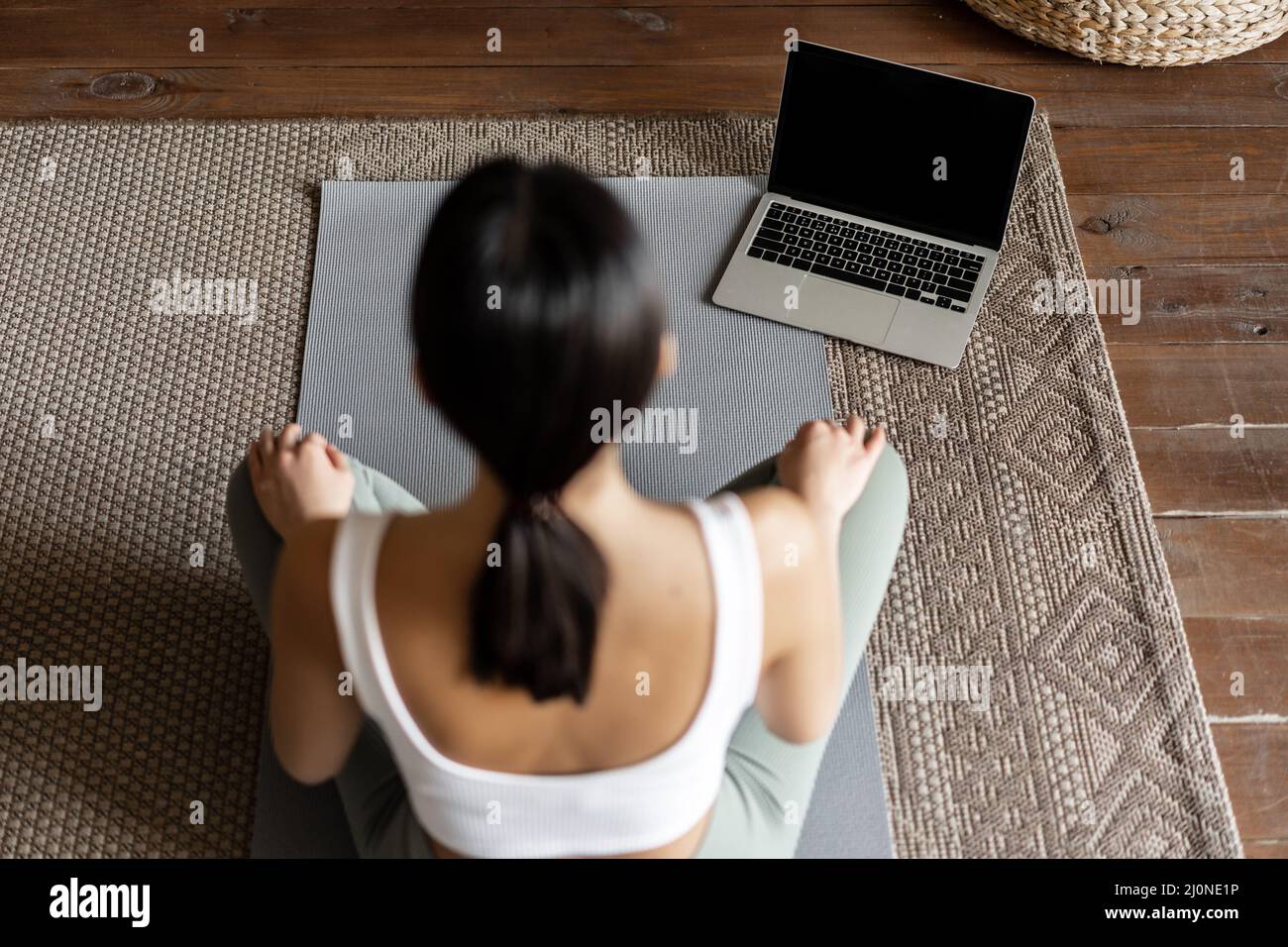 Mindfulness and meditation concept. Rear view of young asian woman meditating at home, following online course on laptop, sittin Stock Photo
