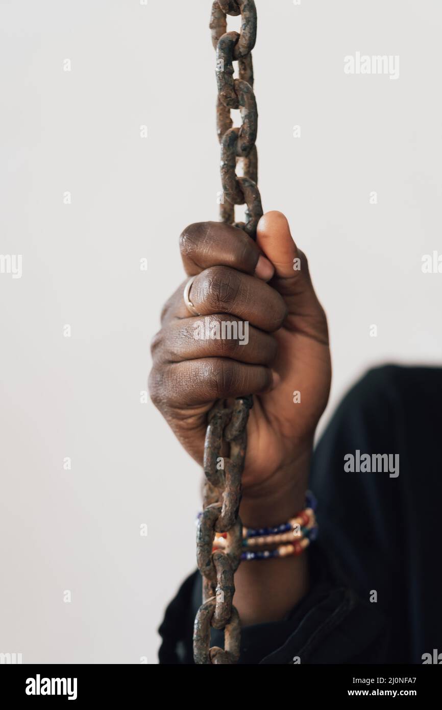Hand of a black African person clinging to a chain, symbol of slavery, exploitation and deprivation of liberty Stock Photo