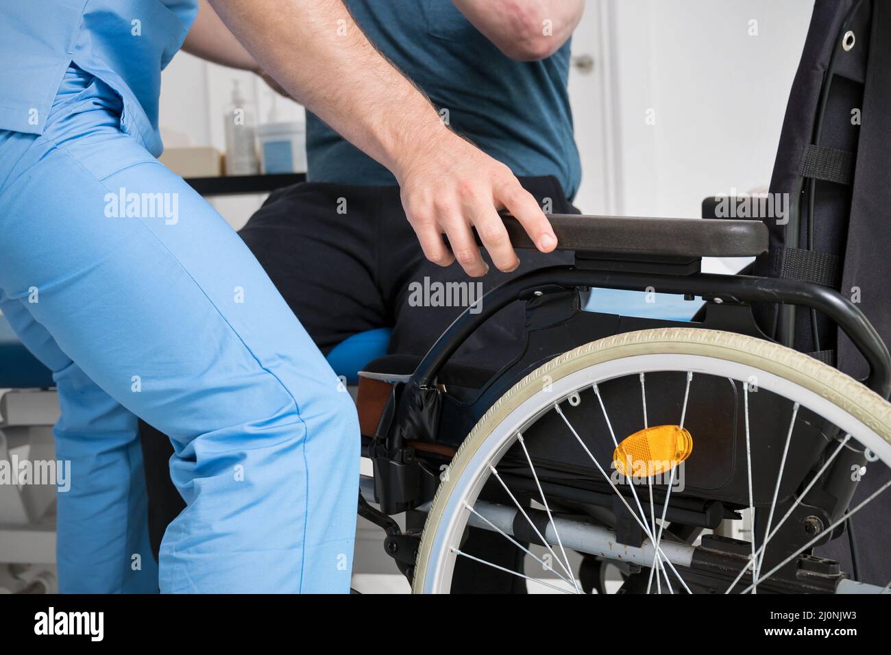 Male Physiotherapist helping a patient with a disability who uses a wheelchair to get up at