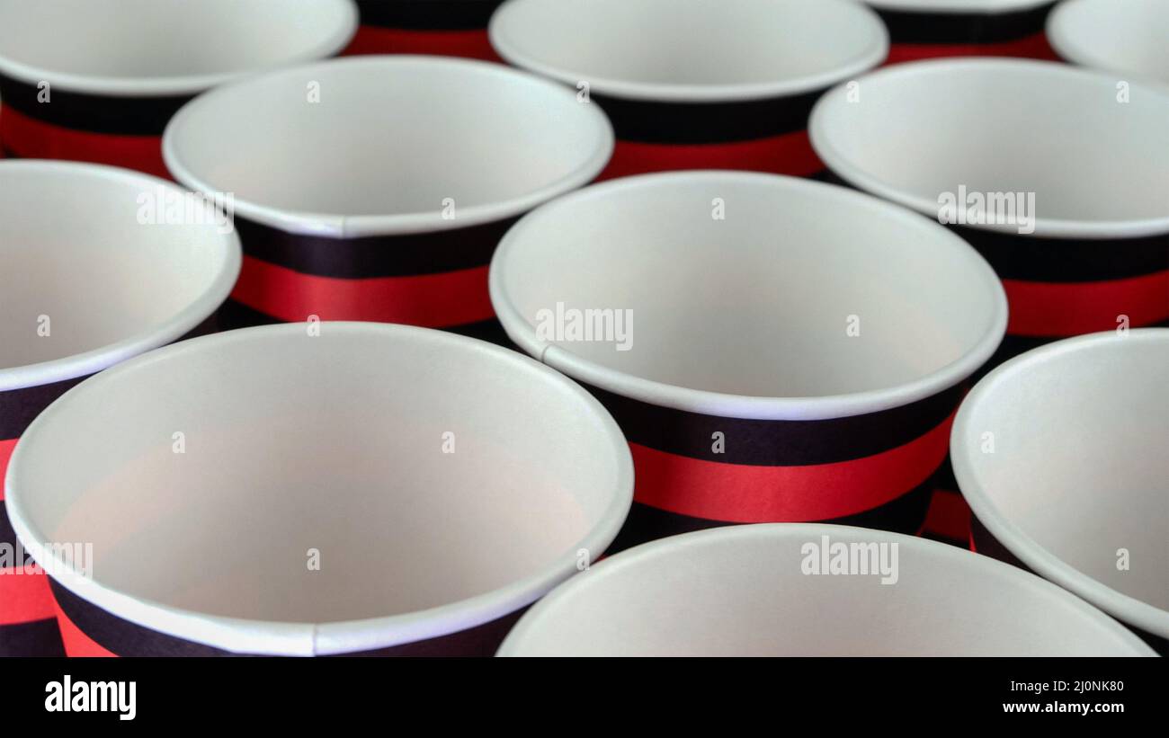 Row of red and black disposable eco friendly paper cup for coffee or hot beverage on dark backdrop. Selective focus. Close-up. Stock Photo
