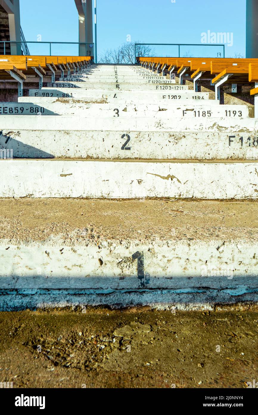Numbered steps in the sport stadium between the wooden seats over the blue sky. Concrete stairs at the empty stadium without the spectators Stock Photo
