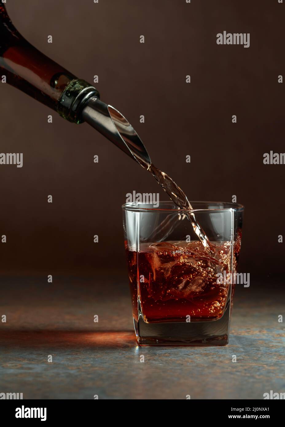 Whiskey is poured from a bottle into a frozen glass with natural ice