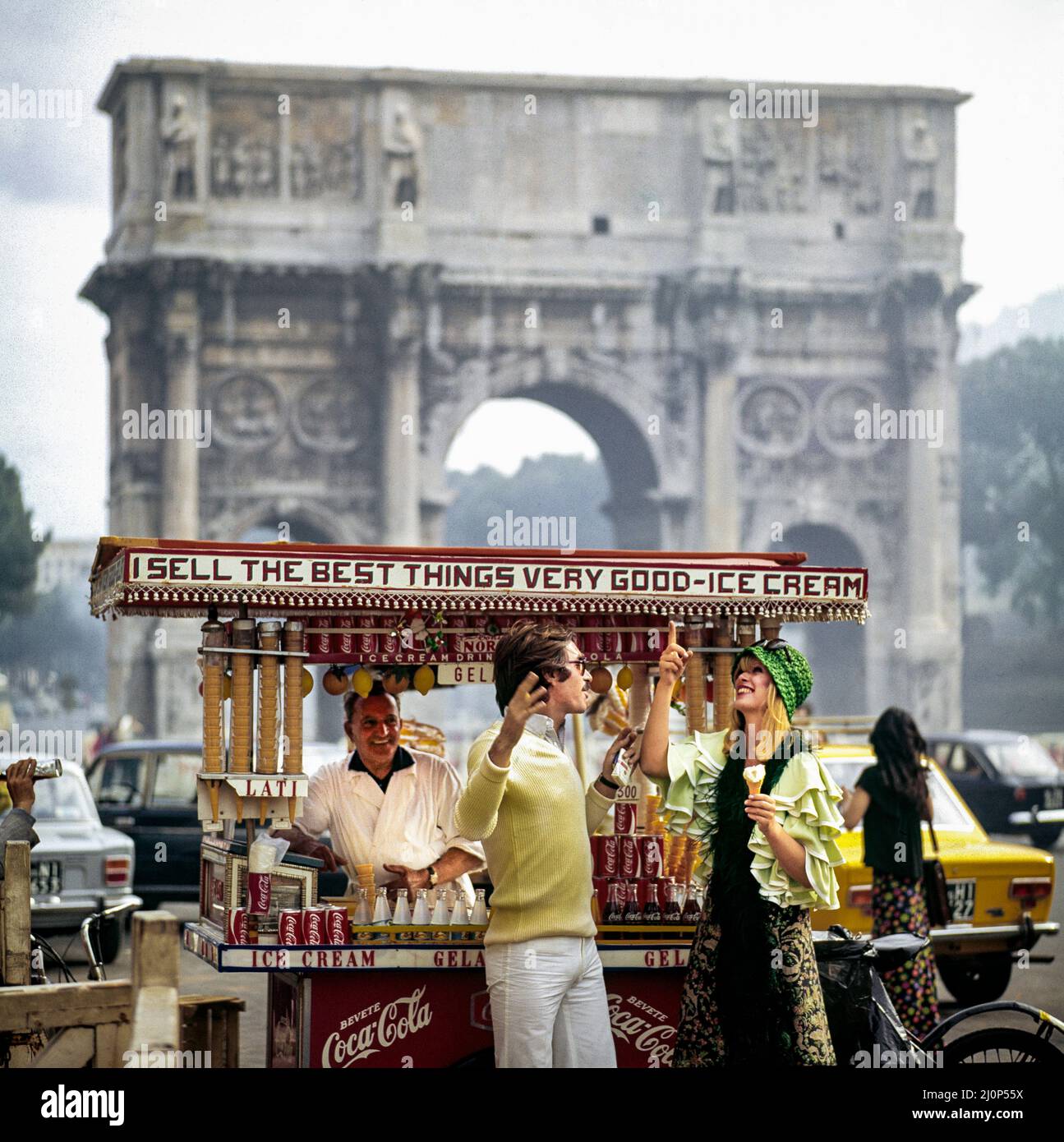 Vintage Rome 1970s, couple having fun by street ice-cream seller in front of triumphal arch of Constantine, Italy, Europe, Stock Photo