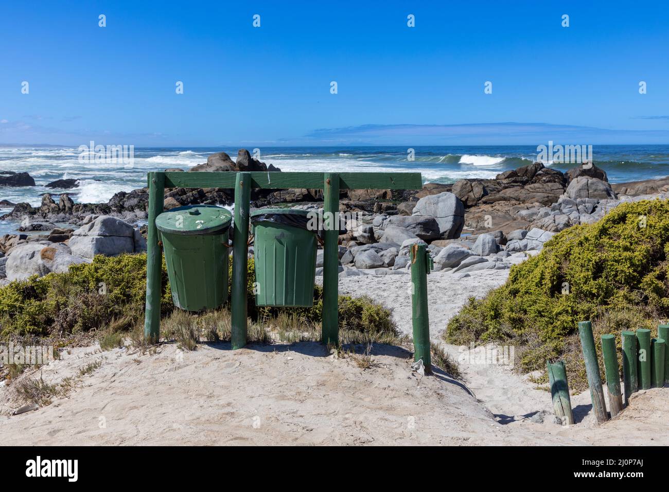 Two green rubbish bins with the ocean behind it. This is in the West