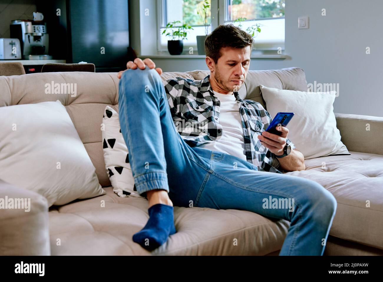 Man using smartphone for browsing social media, resting on sofa at leisure weekend. Male hand touch phone screen, surfing online news Stock Photo
