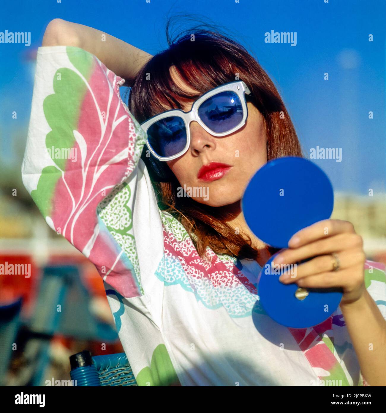 Vintage Italy 1970s, pretty woman with white sunglasses looking into a blue compact mirror checking her make up, Kursaal beach, Lido di Ostia, Europe, Stock Photo