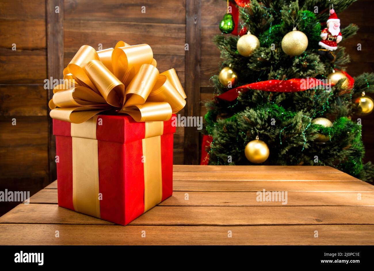 Christmas and New Year Red Box Gift Decorated by Golden Ribbon and Big Golden Loopy Bow. Christmas Tree with Balls, Ribbons, San Stock Photo