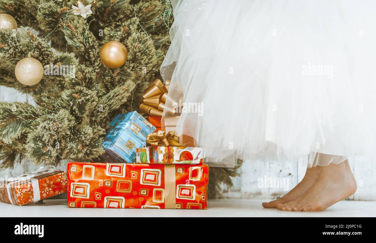 Girl in a White Tutu Skirt is Standing Bare Feet on the Floor by the New Year Tree. Close-up Stock Photo