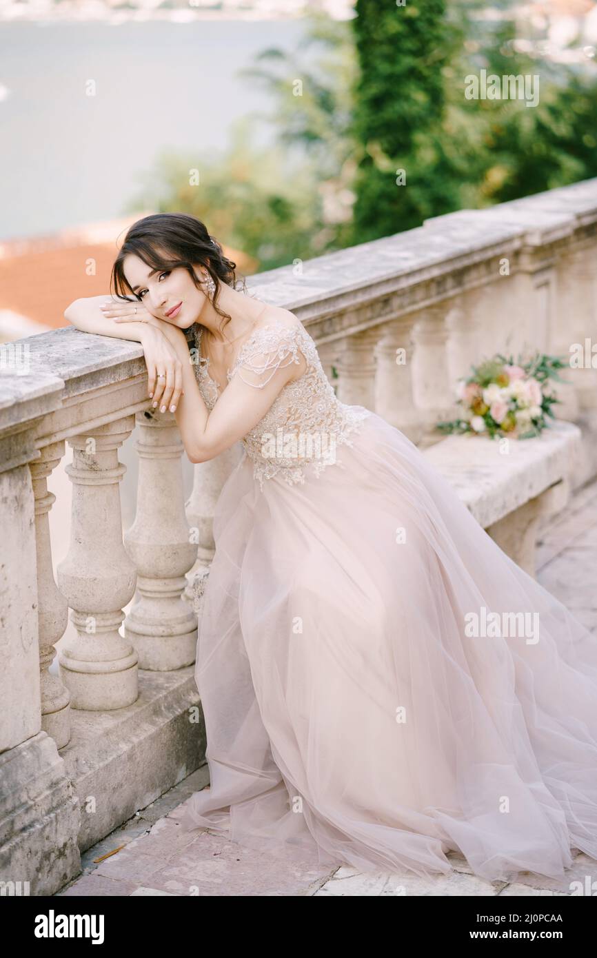 Bride sits on a stone bench with her head resting on a stone balustrade Stock Photo