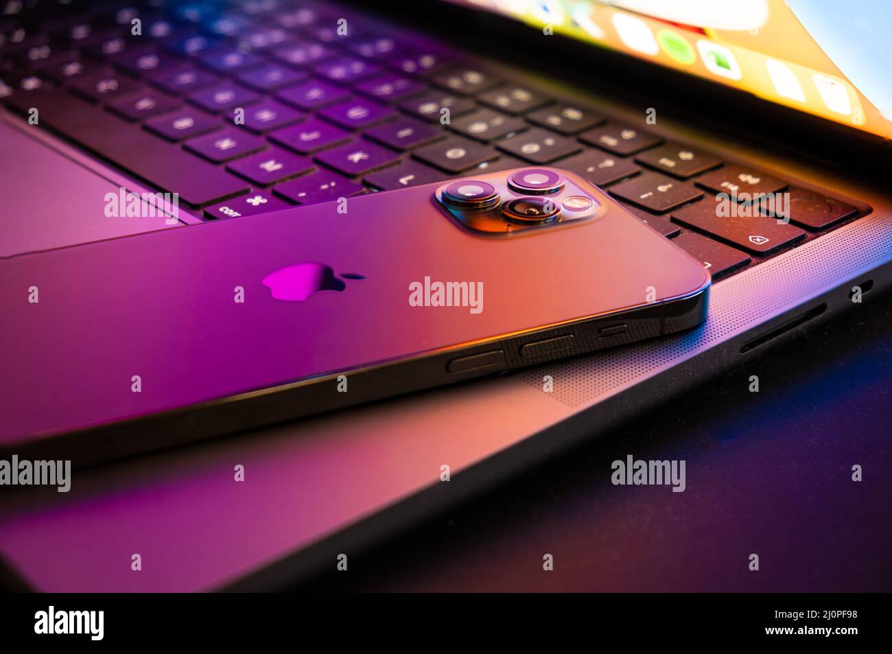 Macbook pro 2021 half open with Iphone 13 lit by retina display Stock Photo
