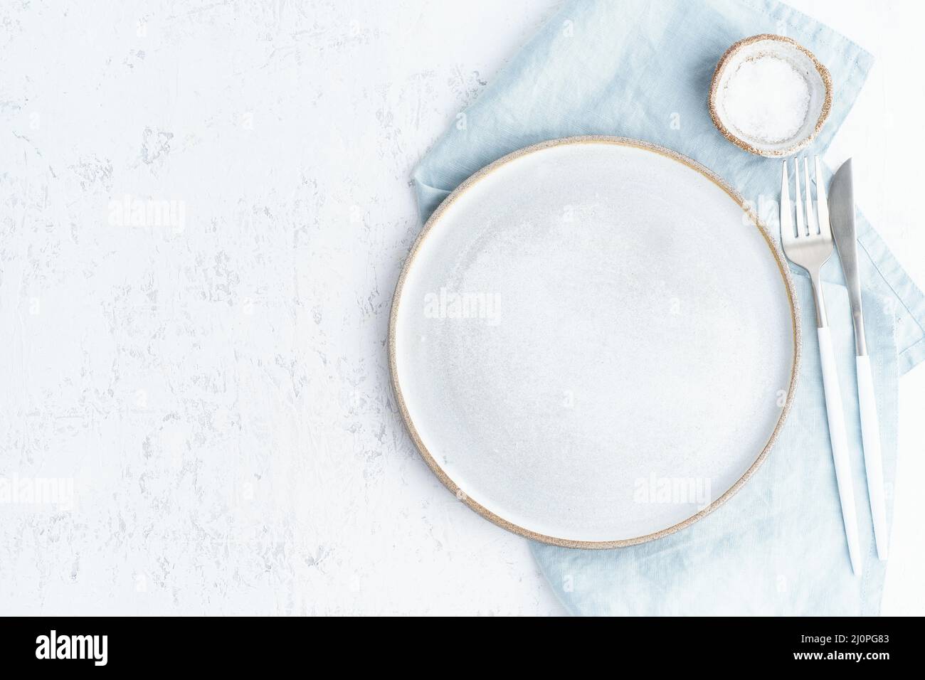 Clean empty white ceramic plate, fork and knife on white stone table
