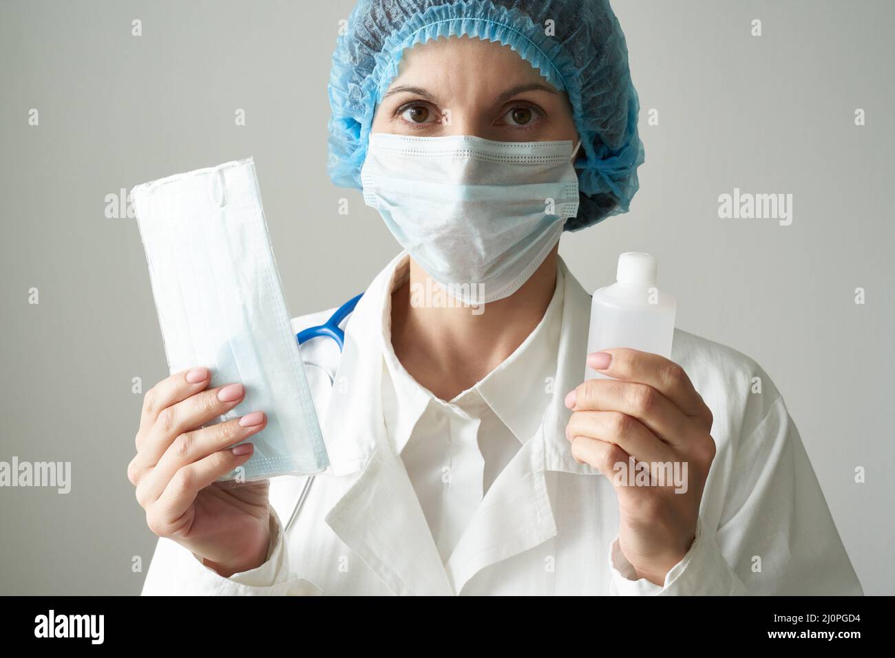Female doctor in medical mask offers mask and disinfectant in bottle to prevent from coronavirus. Stock Photo