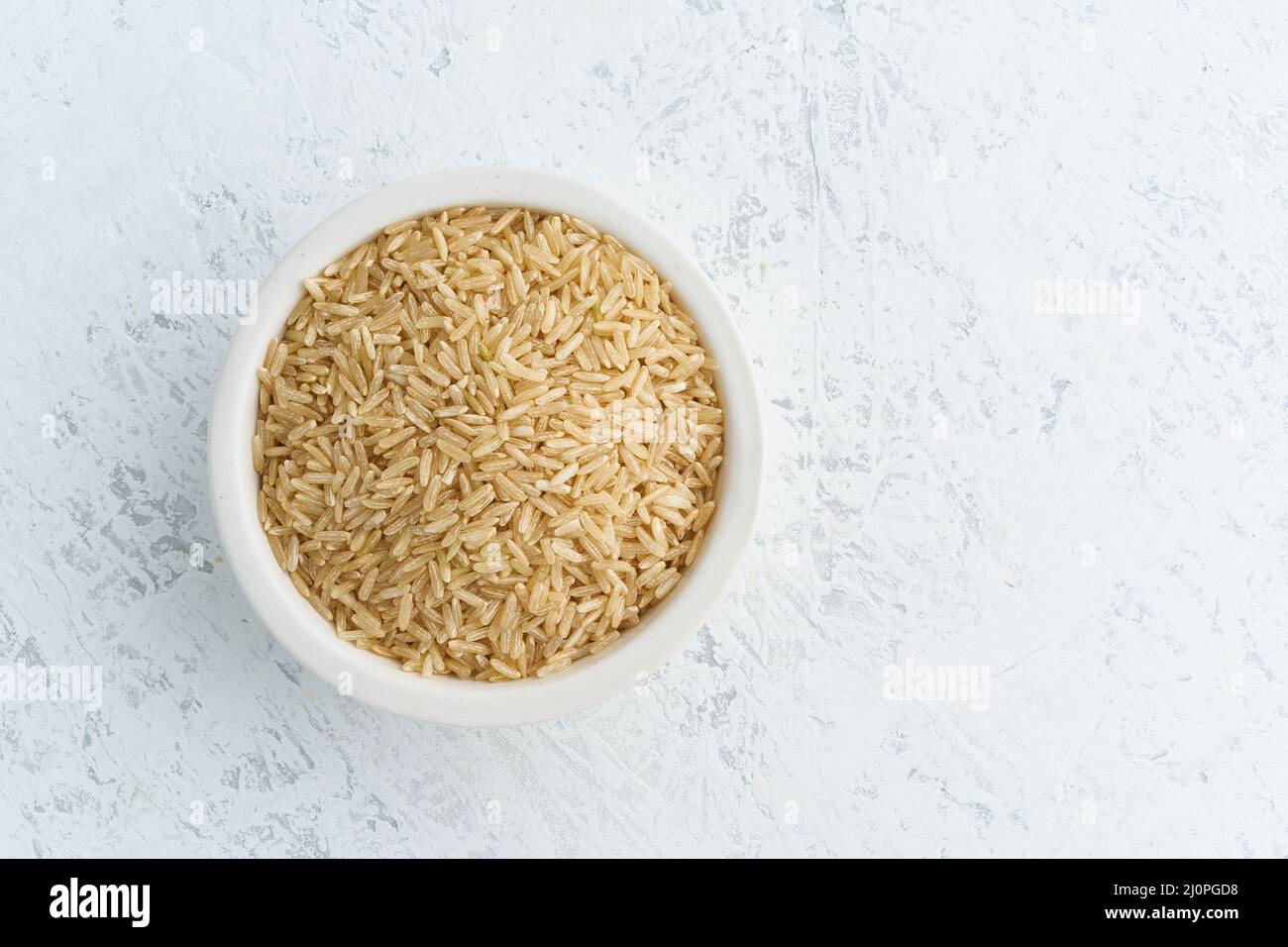 Brown rice in white bowl on white background. Dried cereals in cup, Stock Photo