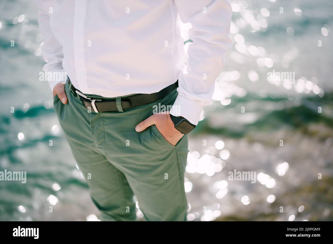 Man in green trousers stands over sparkling water with his hands in his pockets. Close-up Stock Photo