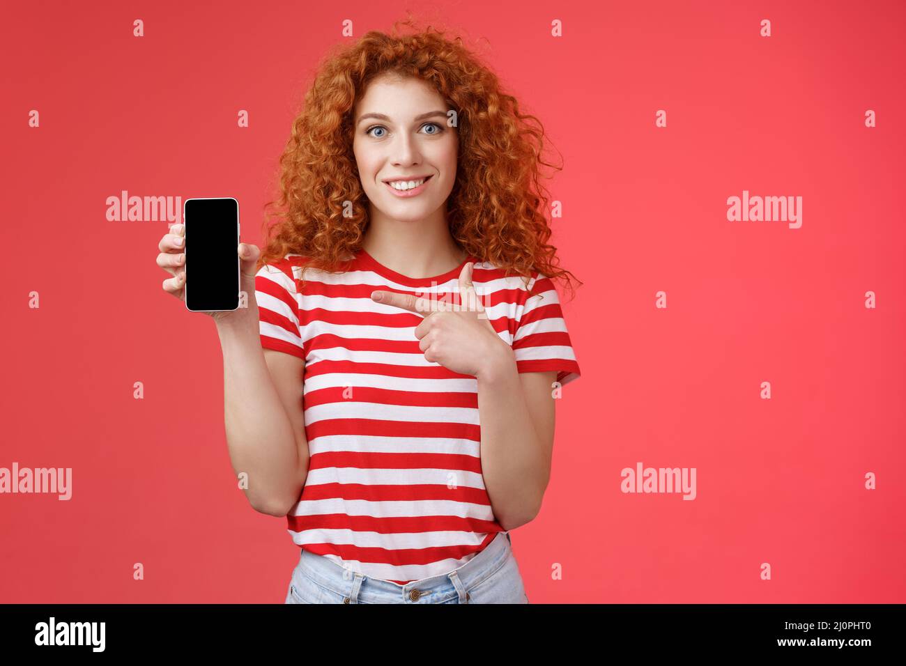 How about this app. Redhead curly friendly cute girl help friend find oufit online store hold smartphone pointing phone screen s Stock Photo