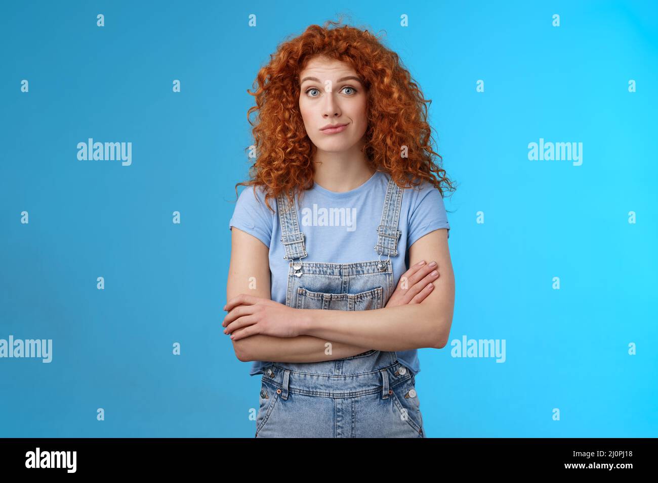 Unsure confused redhead curly woman look perplexed uncertain cross arms chest smirking stare camera full disbelief suspicious do Stock Photo