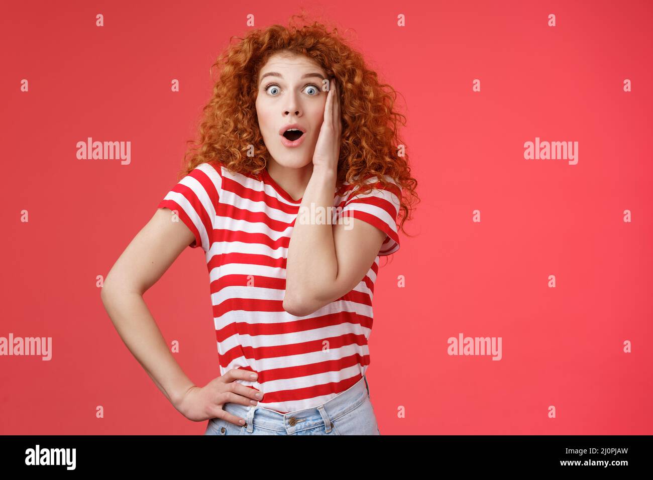 Shocked amused emotive redhead ginger girl curly haircut popping eyes stare camera fascinated impressed open mouth gasping enter Stock Photo