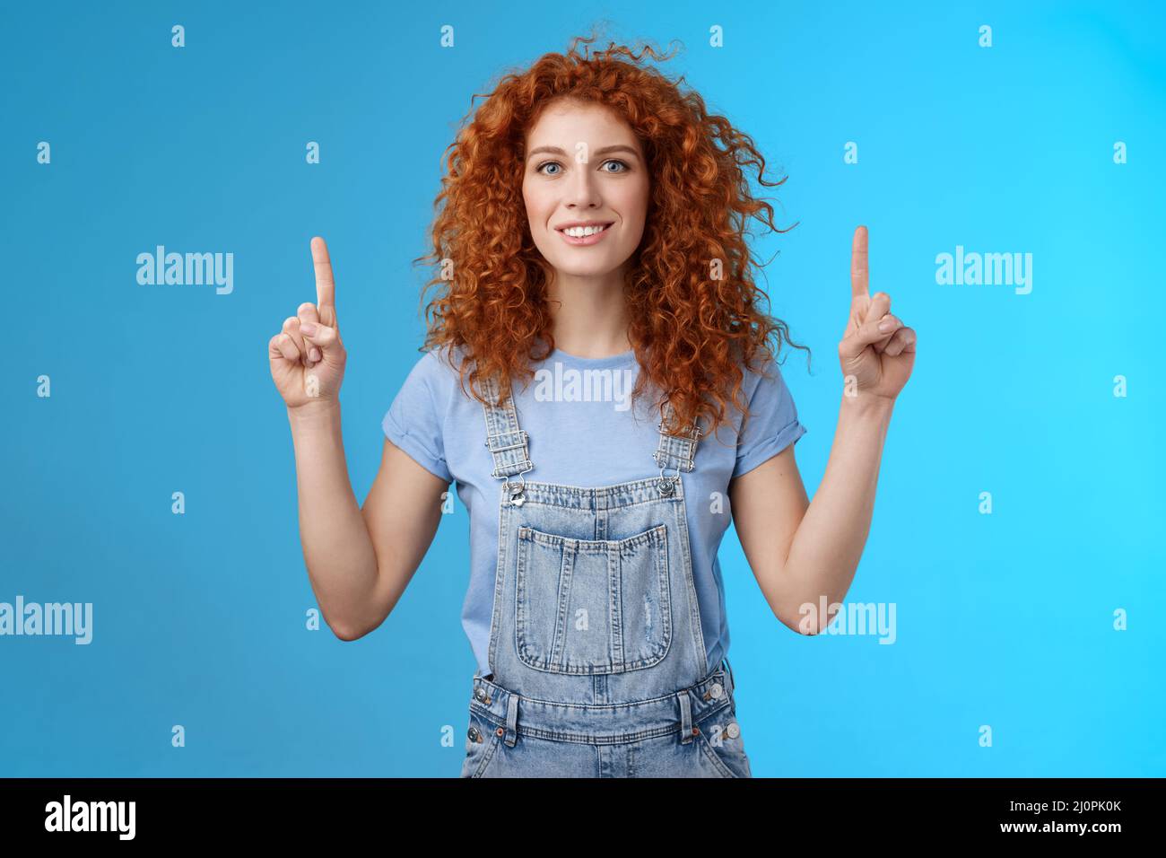 Motivated happy cheerful redhead silly curly woman pointing up inrdex finger smiling charmed impressed excited showing awesome p Stock Photo