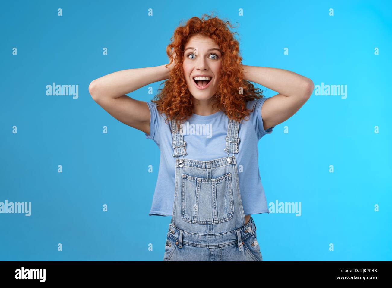Excited amused joyful redhead curly girl having amazing perfect news touch hair astonished stare camera thrilled cheerful overjo Stock Photo