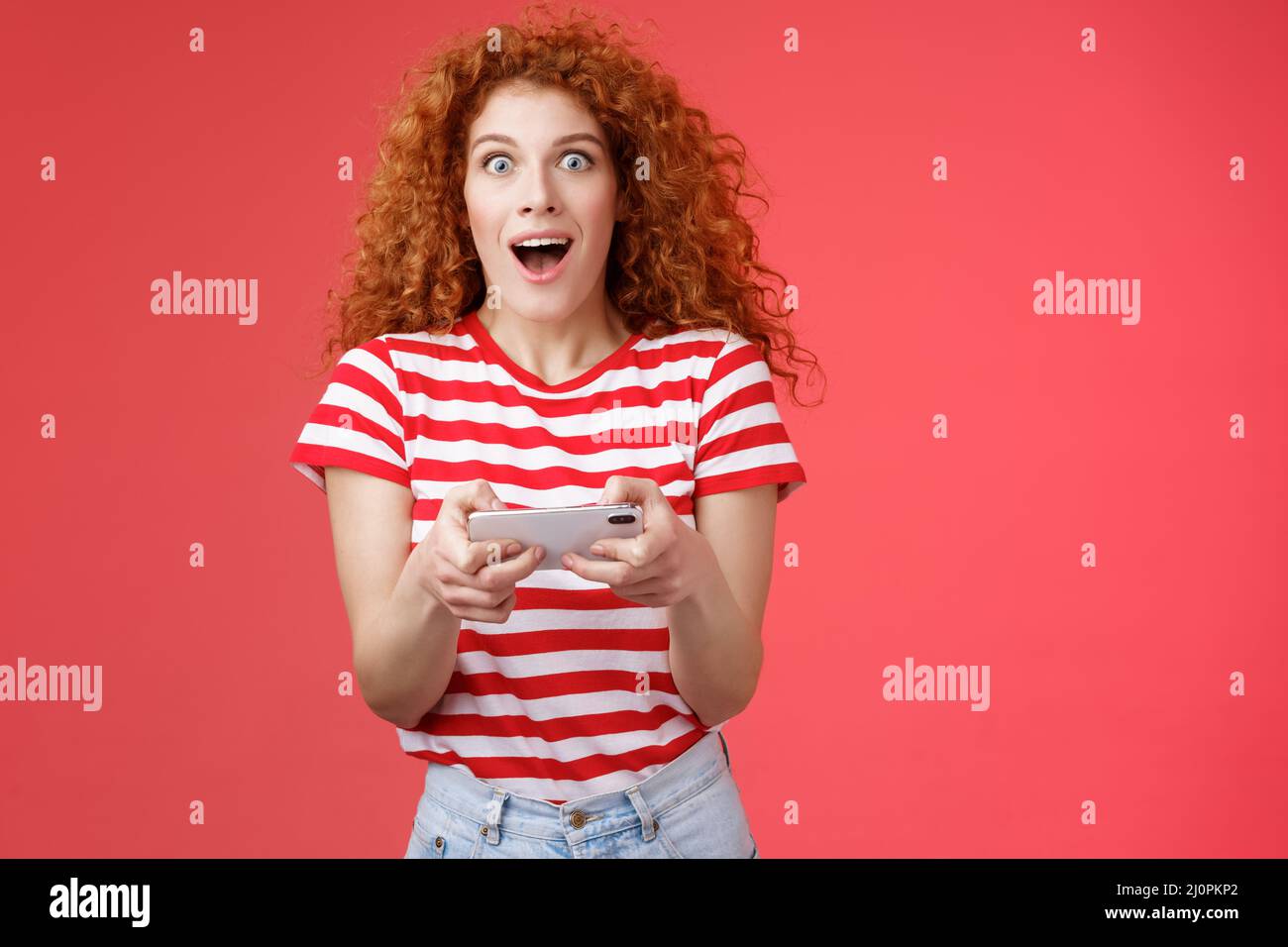 Amused impressed good-looking curly-haired redhead female student unexpectedly win smartphone game look camera astonished gaspin Stock Photo