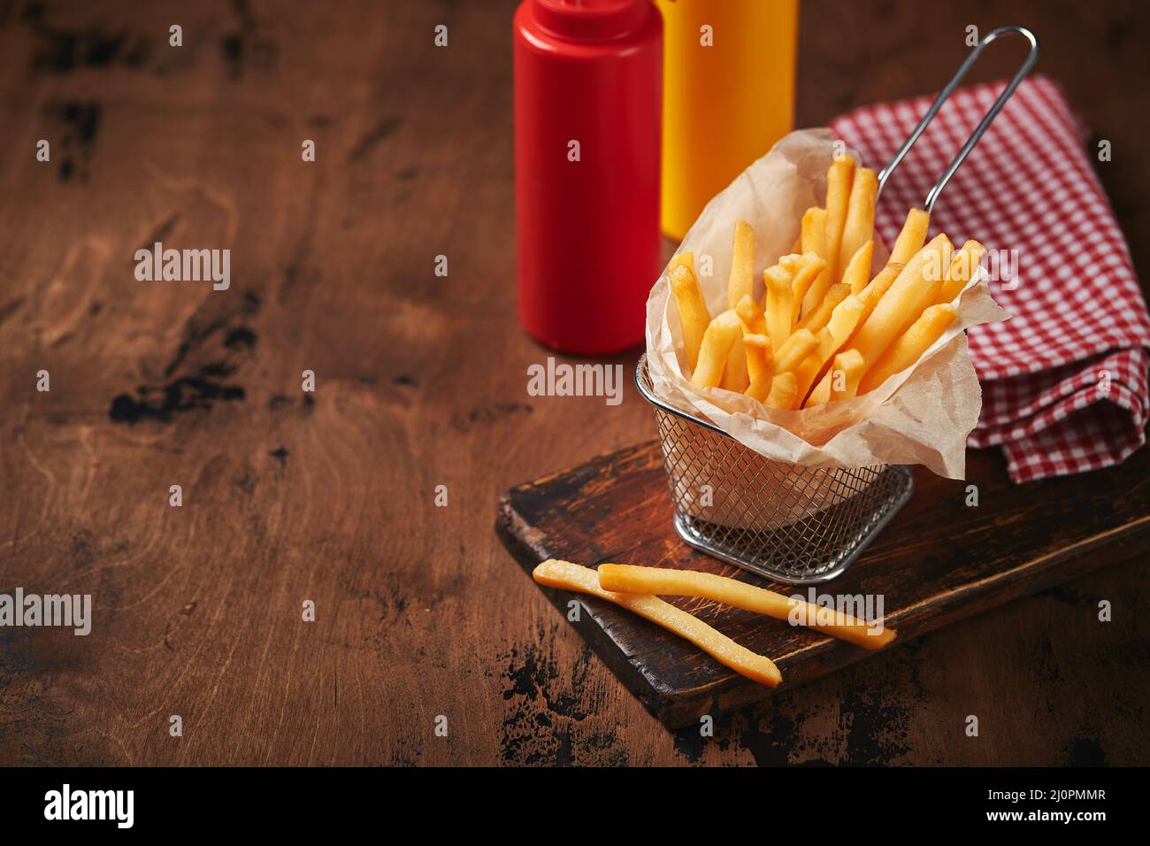 French fries in a metal mesh basket on a wooden board. Fast food concept, american food Stock Photo