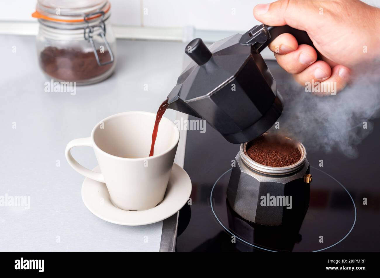 Disassembled coffee maker with one part on the fire and the other serving coffee in a cup. Stock Photo
