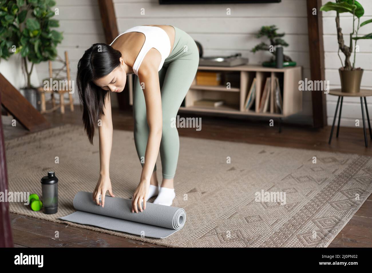 Asian fitness girl finish training,workout at home, rolling floor mat after exercises in living room Stock Photo
