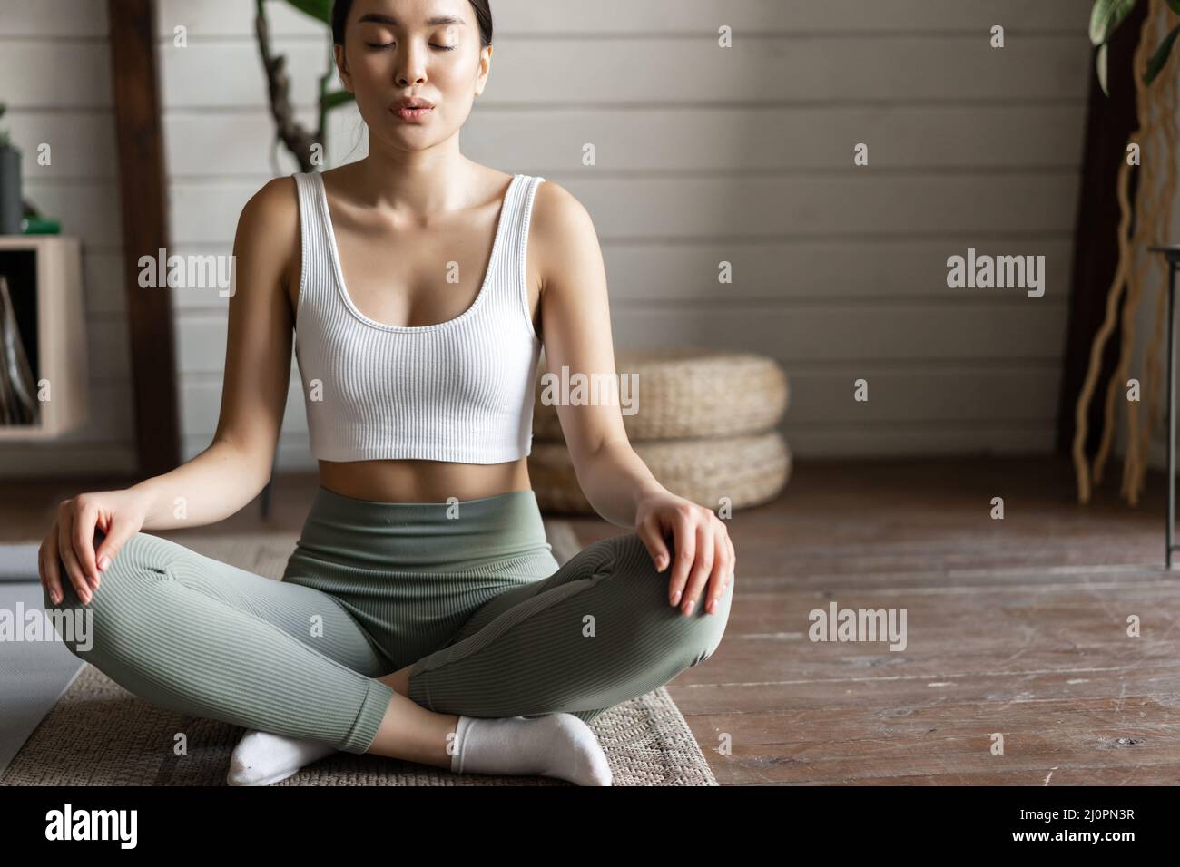 Close up of young asian girl, fitness athlete at home doing workout on floor mat, meditating and stretching, yoga exercises Stock Photo