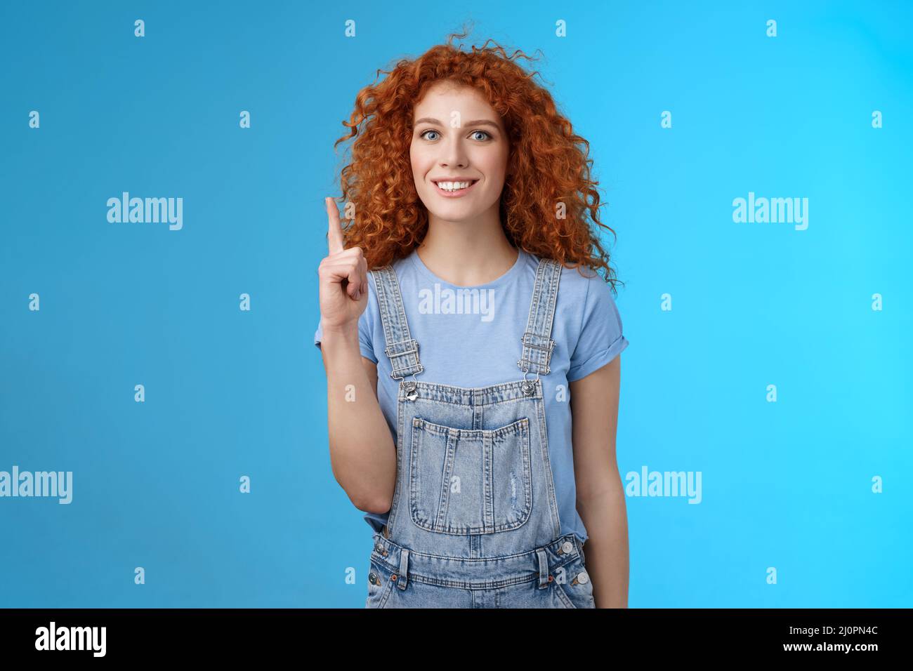 Cheerful cute energized redhead curly girl wear denim overalls book summer vacation trip offer good offer link pointing raised i Stock Photo