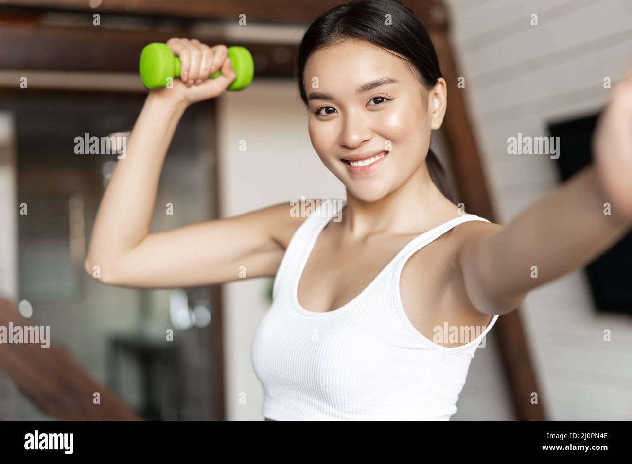 Smiling korean girl taking selfie with dumbbell, workout at home during pandemic, wearing activewear Stock Photo