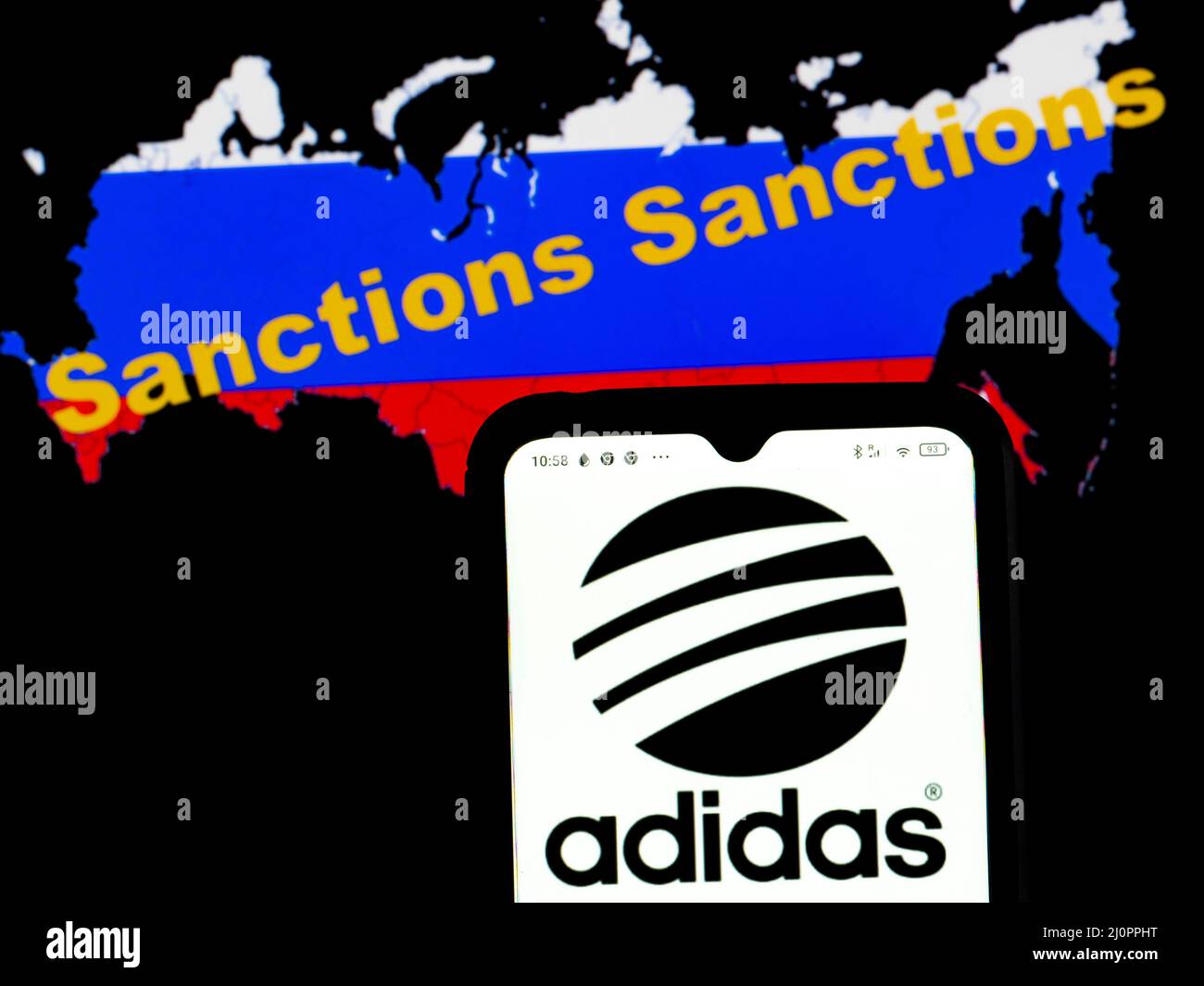 In this photo illustration, the Adidas logo is displayed on a smartphone  screen with a Russian flag in a form of a map of the country with  inscription Sanctions in the background. (