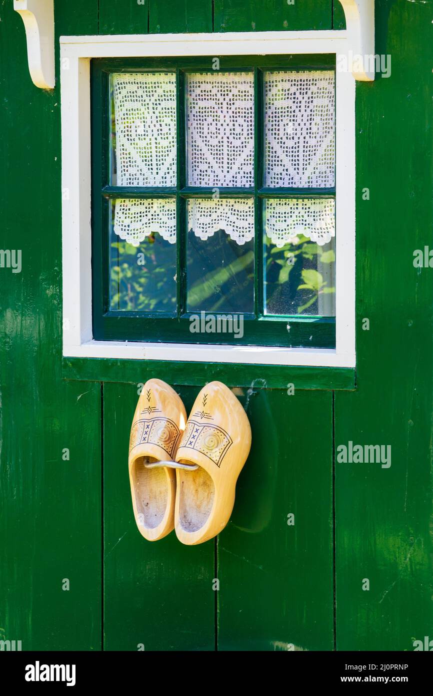 Typical example of Dutch culture. Wooden clogs hanging on green wooden house with window with crochet curtain Stock Photo