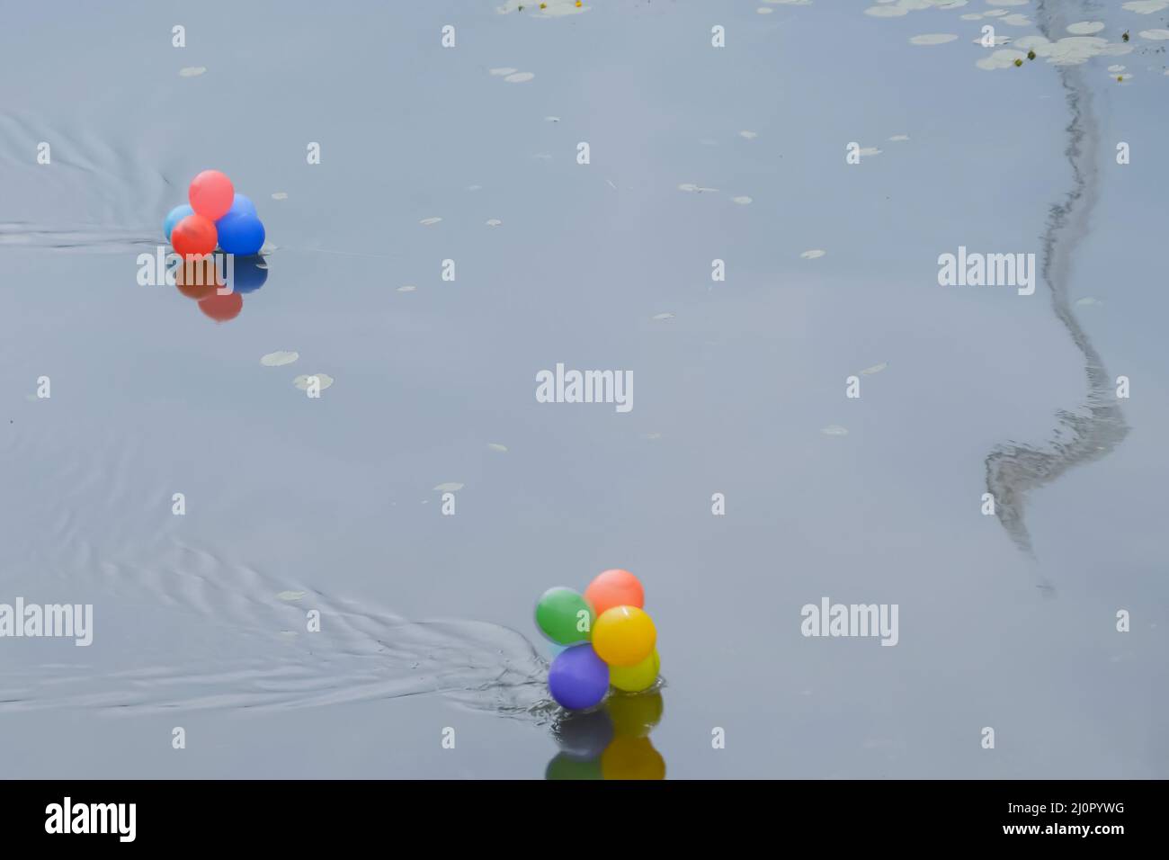 Colorful helium balloons floating in river - water pollution Stock Photo