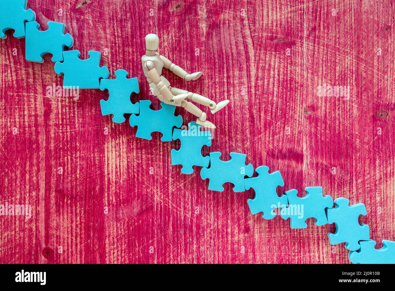 Wooden man sitting on the stairs made of blue puzzle Stock Photo