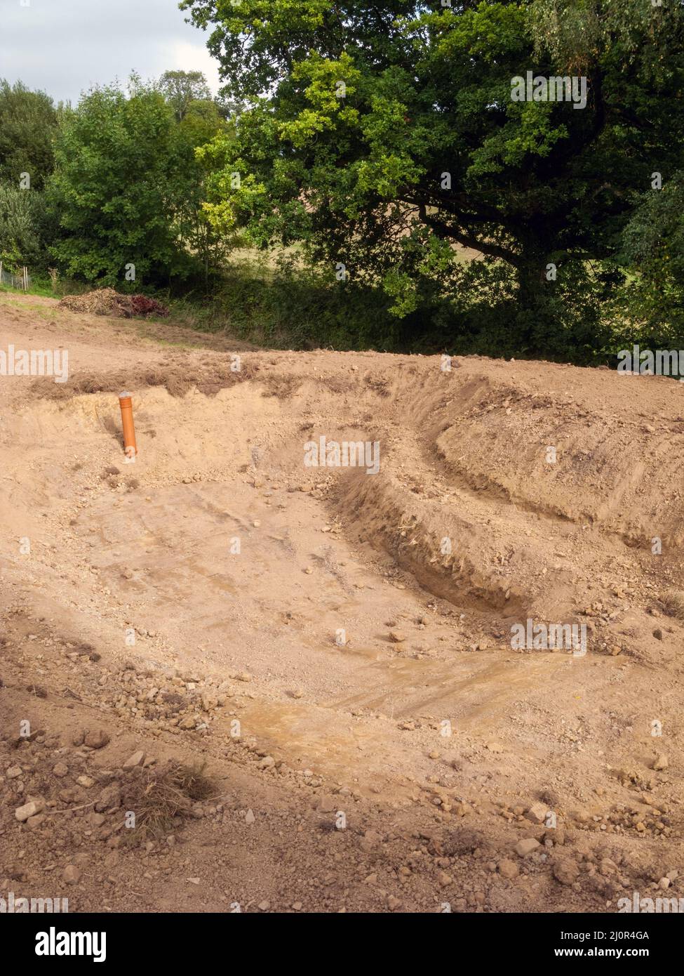 UK, England. Pond construction; 10 x 5 meters. Stage five - digging down to 1.5 meters & shelving bank on one side. Overflow installed. Stock Photo