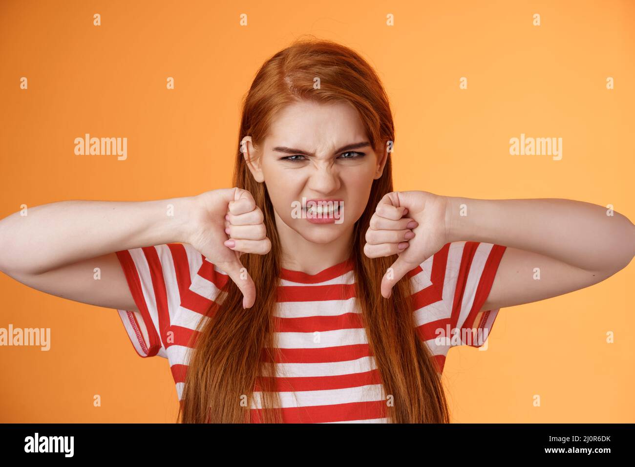 Displeased unhappy redhead female viewer frowning disappointed, give bad feedback watch awful movie, show thumbs-down hateful gr Stock Photo