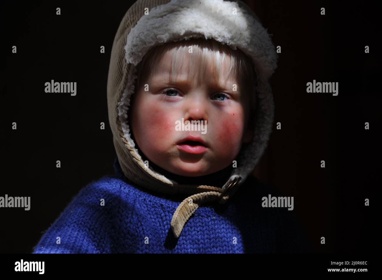 young boy in ray of dappled sunlight with blue grey eyes and jumper