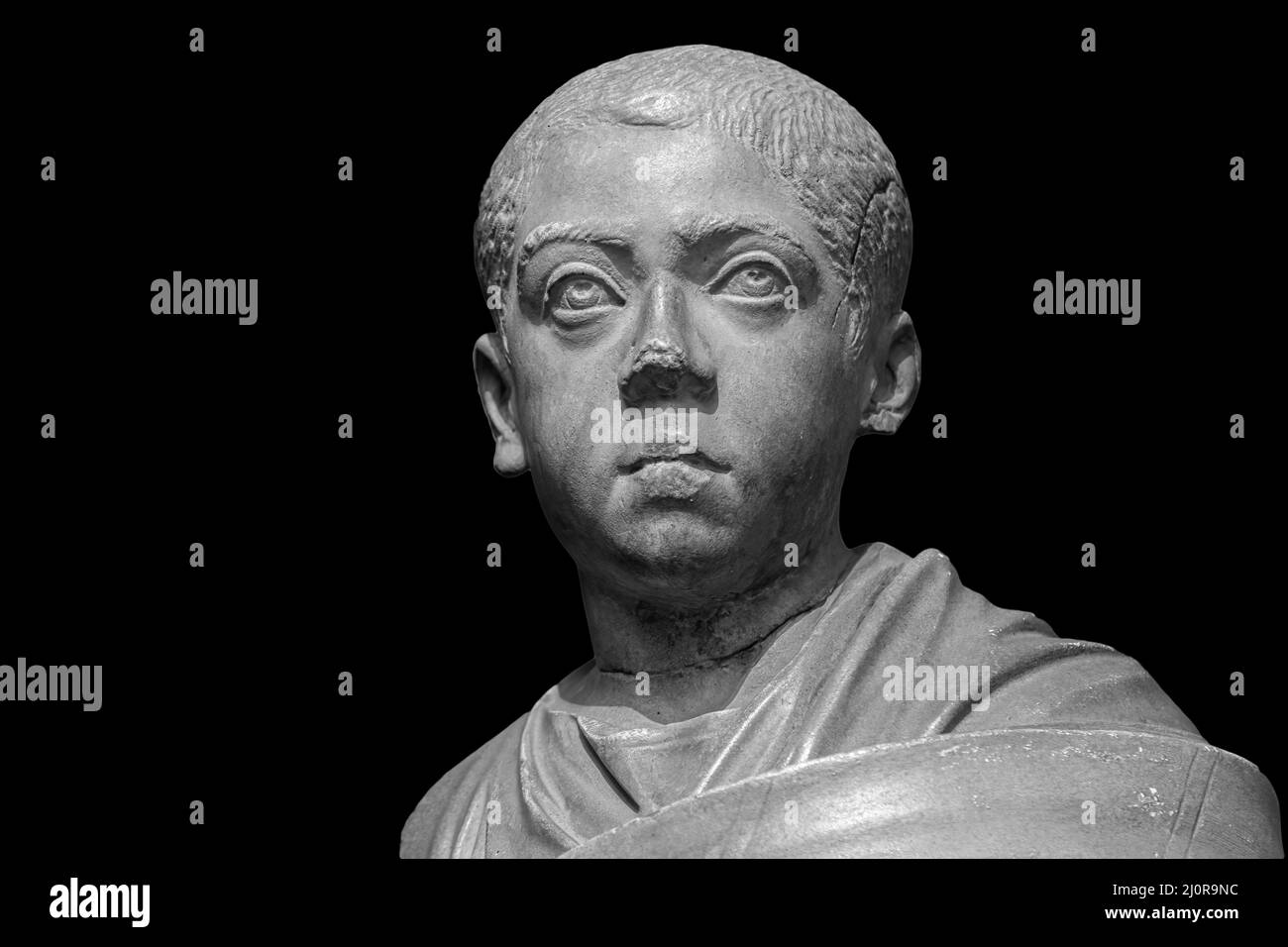 Boy in toga. Head of roman boy statue. Ancient sculpture isolated on black background. Classic antiquity young man man portrait Stock Photo