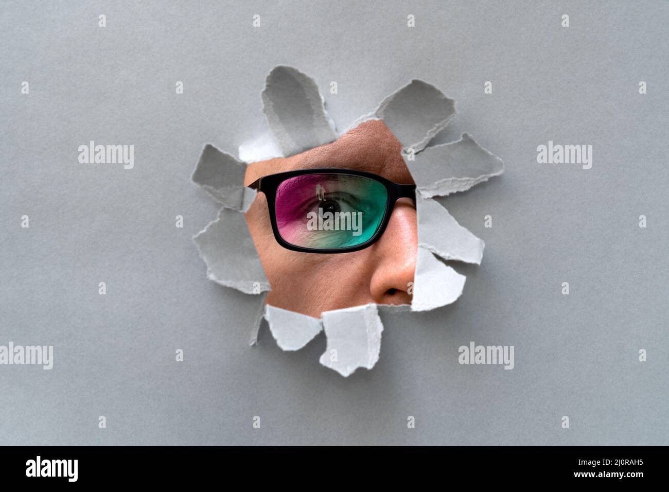 Man in glasses peeping through hole on paper Stock Photo