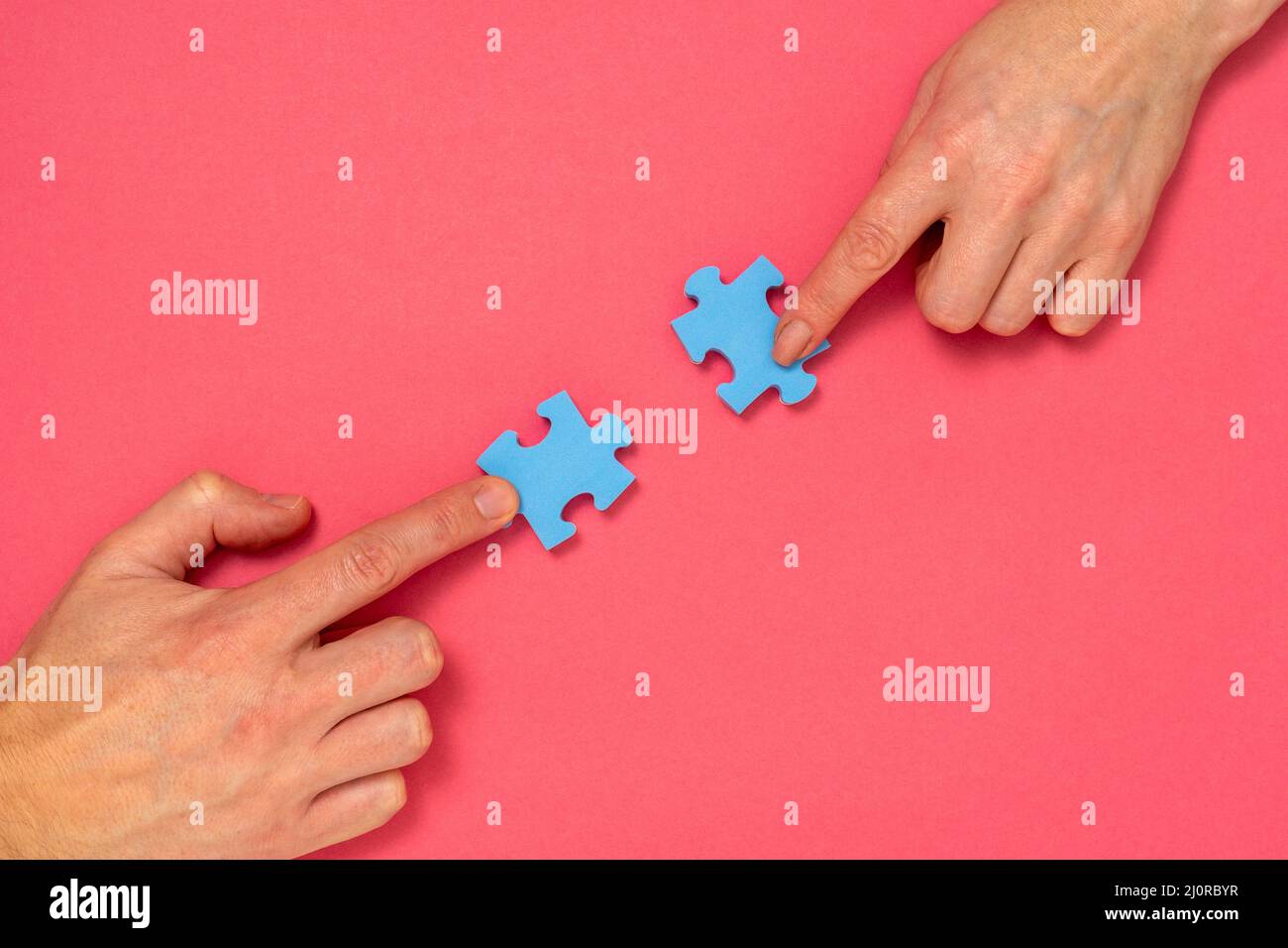 Hands of woman and man matching pieces of blue jigsaw puzzle on pink background Stock Photo
